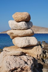 A tower of stones on Ftenagia beach at Emborio on the Greek island of Halki. The uninhabited island of Nissos is in the background.