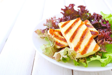 green salad with fried halloumi cheese in a white plate on a white wooden background