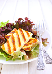 green salad with fried halloumi cheese in a white plate on a white wooden background