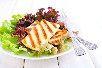 green salad with fried halloumi cheese in a white plate on a white wooden background