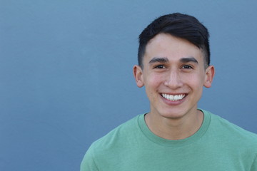 Close up portrait of a young hispanic teenager man looking at camera with a joyful smiling expression, against a blue background. Teenager being confident and smart.