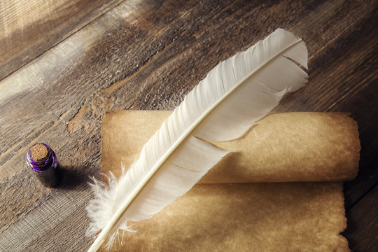 Writing concept. Closeup of scroll and quill near inkstand on wooden table