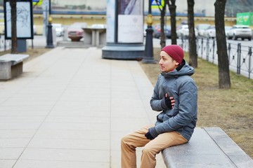 Young tired man sits on a bench in the alley and keeps a hand on the heart.