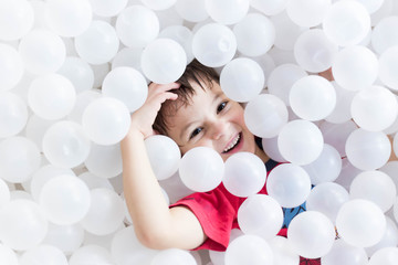 boy hiding under white balls at the playground