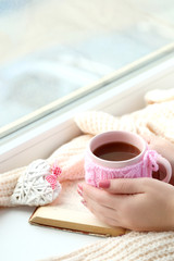 Woman hands holding cup of coffee near the window