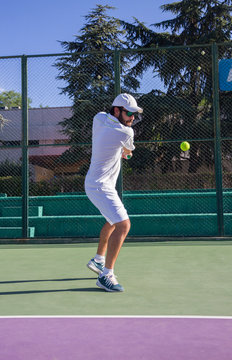 Professional tennis player playing a game of tennis on a court. He is about to hit the ball with the racket. The ball is suspended in the air.