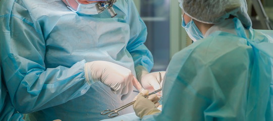 Surgical team performing cosmetic surgery on breasts. Breast enlargement, enhancement. Surgeon holding instruments during medical procedure in hospital operating room. Mammaplasty