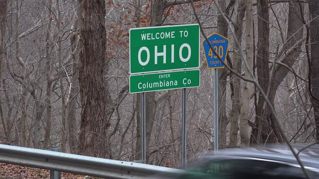 A daytime establishing shot of a Welcome to Ohio road sign.  	