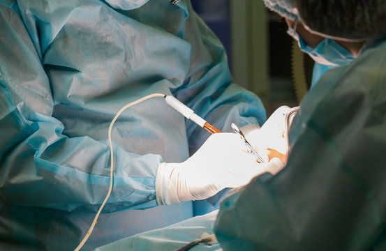 Close-up image of surgeon and his assistant performing cosmetic surgery on breasts in hospital operating room. Doctor holding surgical instrument. Breast augmentation, enlargement, enhancement.