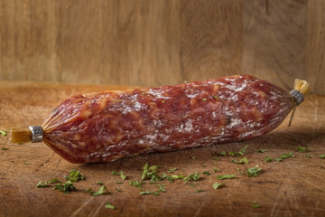 Italian salami on wooden cutting board with herbs