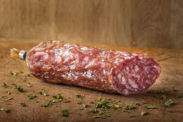Italian salami on wooden cutting board with herbs
