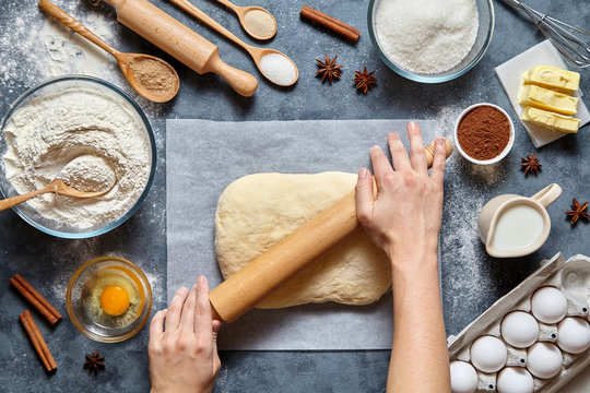 Dough bread, pizza or pie recipe preparation. Female baker hands rolling dough with pin. Food ingridients flat lay on kitchen table. Working with butter, yeast, flour, eggs, pastry or bakery cooking.