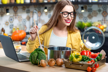 Young smiling woman holding orange pumpkin in the modern kitchen interior with yellow couch