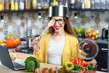 Funny portrait of a young and happy woman with cooking pan and spoon in the kitchen