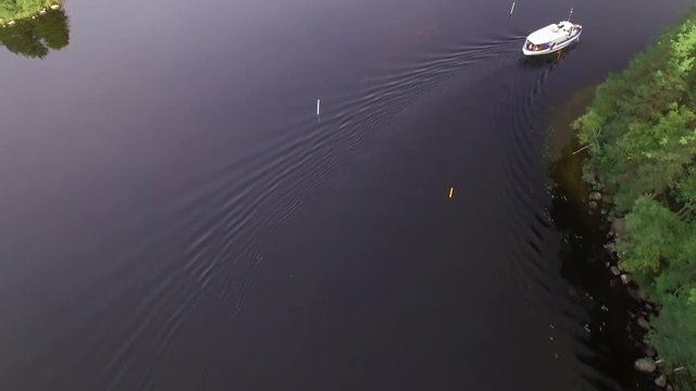 Aerial shot of a small passenger boat turning at a narrow sea lane at a Nordic lake.