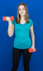 girl with dumpbells on blue background sport concept gym