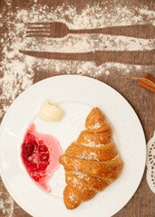 It lies on a plate with croissants, jam and butter, sprinkled with powdered sugar