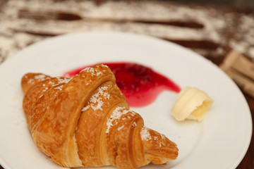 It lies on a plate with croissants, jam and butter, sprinkled with powdered sugar