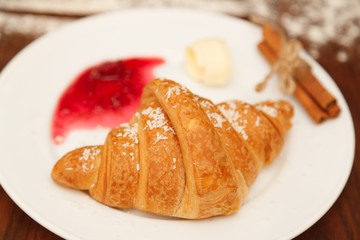 It lies on a plate with croissants, jam and butter, sprinkled with powdered sugar