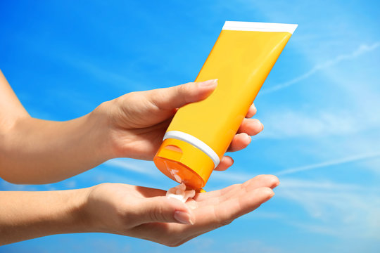 Female hands with sun protection cream on sky background. Skin care concept.