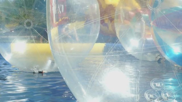 Large inflatable transparent water balls sliding on the water of opened swimming pool