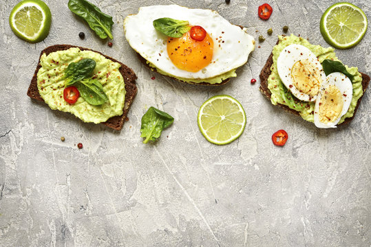 Assortment of avocado toasts on a concrete or slate background.T