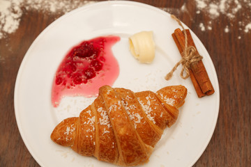 It lies on a plate with croissants, jam and butter, sprinkled with powdered sugar