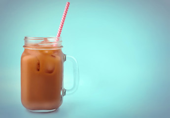 Jar of iced coffee with milk and straw on blue background