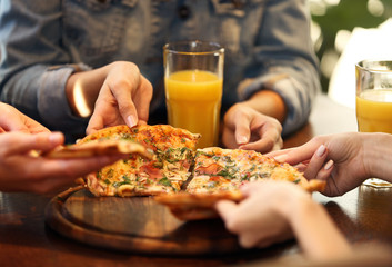Friends taking slices of tasty pizza from plate, close up view