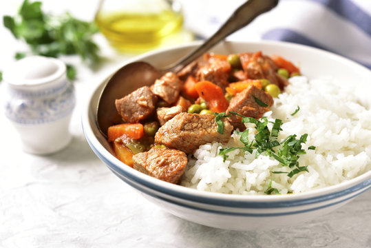 Veal stew served with rice on a light concrete background.