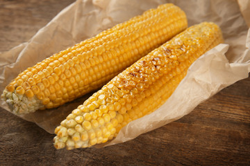 Tasty grilled corncobs on wooden table, close up view
