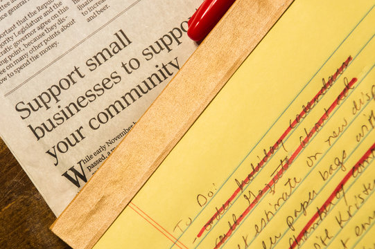 Small Business Article And To Do List  With Several Completed Items Crossed Off With Red Ink. The Red Marker Cap Rests On The Newspaper. 