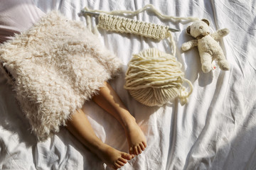 Fototapeta na wymiar legs a little girl lying on the bed bedroom, covered with furs, lie next to a ball of wool for knitting alpaca, needles and teddy bear