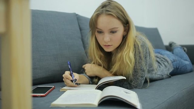 young girl student doing homework at home on the couch