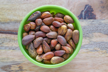 Unshelled pine nuts in green bowl on wooden surface