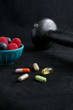 Weight loss plan: dumbbell, berries and dietary supplements on black surface