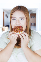 Overweight woman eats donut at home