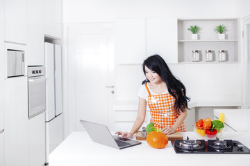Woman cooking and using laptop in kitchen