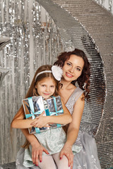 Mother and daughter are waiting for Christmas. Mom dressed fairy fairy hugs daughter. Girl holding two gifts. Happy parenting and childhood. Family holidays.
