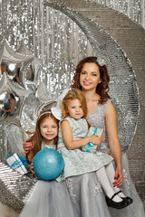 Mother and daughters are waiting for Christmas. Mom dressed fairy fairy embraces daughters. Girls holding a gift in their hands. Happy parenting and childhood. Family holidays.