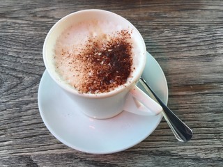 Cappuccino coffee in white cup and spoon on wooden table