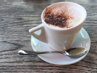 Cappuccino coffee in white cup and spoon on wooden table
