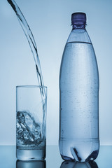 water poured in glass and bottle on blue background
