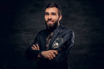 A bearded man dressed in a suit holds vintage 8mm video camera.