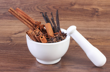 Fragrant anise, cloves, cinnamon and vanilla sticks in mortar on rustic board