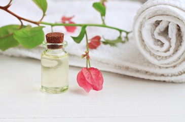Essential oil glass bottle extract, delicate pink tropical flower, white towel. Botanical beauty and health care.