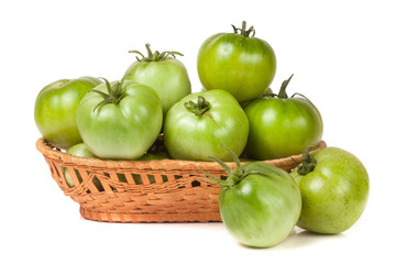 unripe green tomatoes in a wicker basket isolated on white background