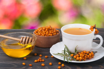 Tea of sea-buckthorn berries with honey on wooden table blurred garden background