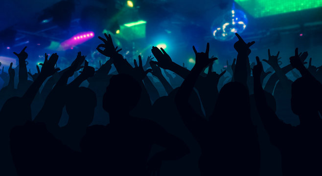 Silhouettes of concert crowd with hands raised at a music disco