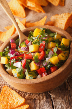 Mexican salsa with mangoes, peppers, cilantro and onion close up in a bowl and nachos. vertical